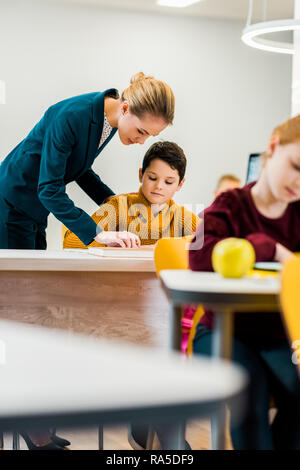 Junge weibliche Lehrer helfen Schüler studieren an Schreibtische Stockfoto