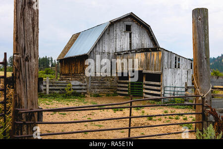 Verfallene hölzerne Scheune durch Zäune, Tor umgeben, und bewachsene Vegetation auf Indianischen Reservation im Sommer in Sioux Falls, South Dakota, USA Stockfoto