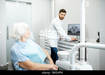 Zahnarzt übersicht Panorama-Aufnahme des Kiefers auf dem Computer an die ältere Frau, die während der Beratung in der Zahnarztpraxis Stockfoto