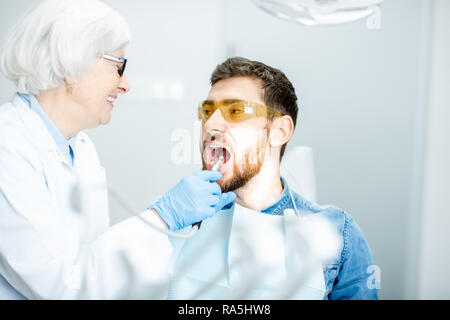 Schöner Mann während der medizinischen Untersuchung mit älteren Frau, Zahnarzt in der Zahnarztpraxis Stockfoto