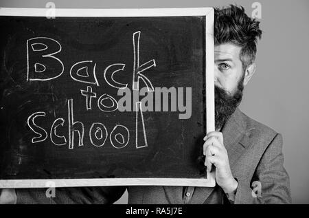 Sind Sie bereit, zu studieren. Lehrer oder Schulleiter begrüßt zurück zur Schule. Lehrer versteckt sich hinter Tafel. Vorbereitung Anfang Schuljahr. Lehrer peeking aus der Tafel über den roten Hintergrund. Stockfoto