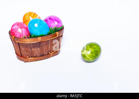 Ein Korb mit grünem Rasen und bunte Ostereier und ein extra Ei auf den Boden, auf weißem Hintergrund mit Kopie Raum gefüllt Stockfoto
