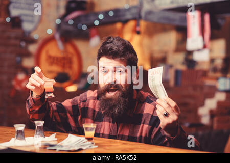 Kerl verbringen Freizeit in der Bar einen Cocktail trinken, defokussiertem Hintergrund. Hipster hält Geld, Bargeld mehr Alkohol zu kaufen. Mann mit betrunkenen Gesicht alleine am Tresen sitzen. Getränke Konzept kaufen. Stockfoto