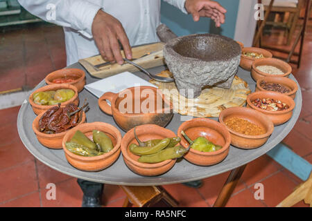 Hand vorbereiten, Salsa in einem Mörser und Stößel, mit vielen kleinen Terra-Cotta Schüsseln mit Zutaten gefüllt, auf einer großen Platte, in Oaxaca, Mexiko Stockfoto