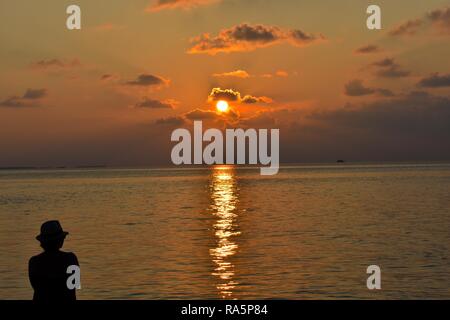 Frau mit Blick auf einen wunderschönen Sonnenuntergang im Paradies auf den Malediven, Indischer Ozean Stockfoto