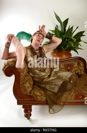 Ältere Frau mittleren Alters, die sich als 1920 Klappe gekleidet Ohnmacht Dame auf der Chaiselongue Stockfoto