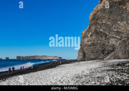 Snowy Abdrücke und Basaltsäulen Formationen entlang Reynisfjara schwarzer Sandstrand, mit Dyrholaey Natural Arch entfernt, in Island [kein Modell Release Stockfoto