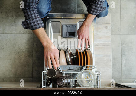 Der Mann schob das schmutzige Geschirr in die Spülmaschine. Stockfoto