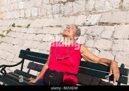 Touristen und Besucher nehmen die Sonne auf Bänken am Rande des Hafens von Porat, Dubrovnik, Kroatien Stockfoto