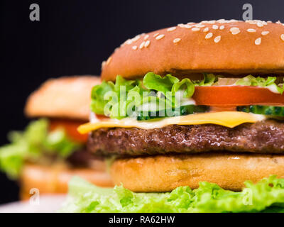 Frische leckere gegrillte Burger auf schwarzen Hintergrund. Fleisch Patty, Tomaten, Gurken, Kopfsalat und Sesam. Fast food Junk Food lifestyle Konzept. Stockfoto