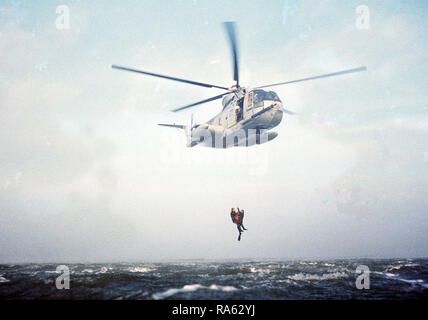 1977 - ein Meer-blick auf eine HH-3 Jolly Green Giant Hubschrauber mit einem Recovery hoist zwei pararescuemen aus dem Wasser vor der Küste von Kalifornien zu heben. Die Männer, von der die 129 für Luft- und Raumfahrt Rescue & Recovery Gruppe der Air National Guard, beteiligen sich an einer Praxis Rescue Mission. Stockfoto