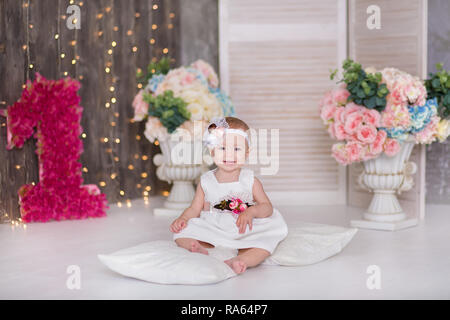 Cute Baby Mädchen 1-2 Jahre alten sitzen auf dem Boden mit rosa Luftballons im Zimmer über Weiß. Isoliert. Geburtstag. Feier. Happy birthday Baby, ein wenig Stockfoto