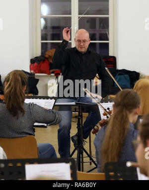 Schwerin, Deutschland. 19 Dez, 2018. Dirigent Stefan Kerber und der Schweriner Youth Symphony Orchestra im Chaos die Probe, die erste Probe des Orchesters. Das Orchester mit über 60 Mädchen und Jungen zwischen 12 und 19 spielt Stücke für ein neues Programm für das erste Mal im Alter. Schätzungen zufolge mehr als 150.000 Kinder spielen in etwa 5000 Kinder- und Jugendorchestern in Deutschland. Sie reichen von einfachen Spielen Kreisen zu vollständigen Symphonieorchester. Quelle: Bernd Wüstneck/dpa/Alamy leben Nachrichten Stockfoto