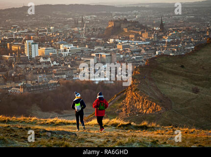 Edinburgh, Schottland, Großbritannien. 2. Januar 2019. UK Wetter, Touristen genießen die Aussicht von Arthur's Seat Gipfel in Holyrood Park gleich um Sonnenuntergang über Salisbury Crags, obwohl die Temperatur minus 1 Grad nach einer Nacht von minus sechs Grad. Stockfoto