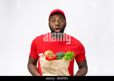 Junge afrikanische amerikanische Mann, Lebensmittelgeschäft Paket in den Händen mit schockierenden Gesicht. Über grauer Hintergrund isoliert. Stockfoto