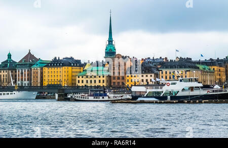 Panoramablick vom Boot aus am Wasser Häuser in Gamla Stan, Touristenbooten und Skeppsholm Skeppsholmsbron (Brücke) mit goldener Krone in Stockholm Stockfoto