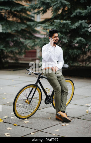 Hübscher junger indischer Mann mit Anzug am Telefon sprechen beim Gehen mit dem Fahrrad morgens zur Arbeit. Stockfoto