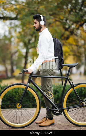 Indische jungen Mann Pendeln zum Büro mit dem Fahrrad in den frühen Morgenstunden. Mann, office Bag und drahtlosen Kopfhörer mit dem Fahrrad. Stockfoto