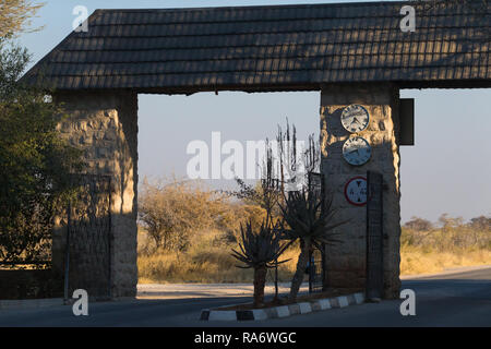 Okaukuejo Rest Camp Gatter öffnen und die Zeiten der Schließung und Öffnung auf eine Uhr auf der Steinmauer in Etosha National Park, Namibia Stockfoto