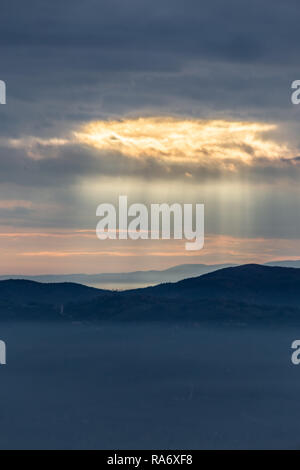Sonnenstrahl scheint durch Wolken über die Berge und ein Meer von Nebel Stockfoto