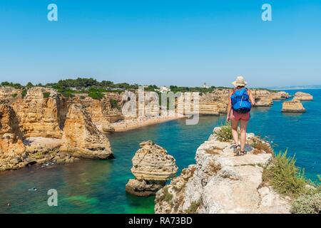 Junge Frau, die auf den Felsen, mit Blick auf das türkisfarbene Meer, Strand Praia da Marinha, Schroffe Felsenküste von Sandstein Stockfoto