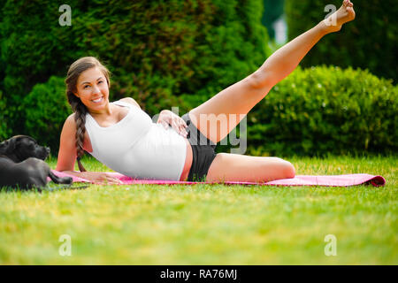 Schwangere junge Frau Durchführung Seite liegende Bein anheben In Park Stockfoto