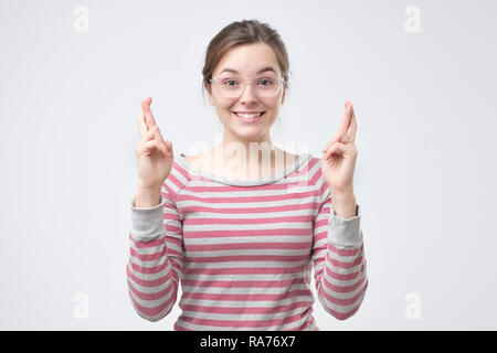 Mädchen in aufgeregt, abergläubisch und naiv aussehen, die Daumen halten. Stockfoto