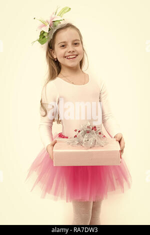 Urlaub, Geburtstag, Jubiläum zu feiern. Kind mit Blume im langen blonden Haare isoliert auf Weiss. Vorhanden oder Geschenk geben. Mädchen ballerina Lächeln mit Box im rosa Tutu Rock. Boxing Day Konzept. Stockfoto