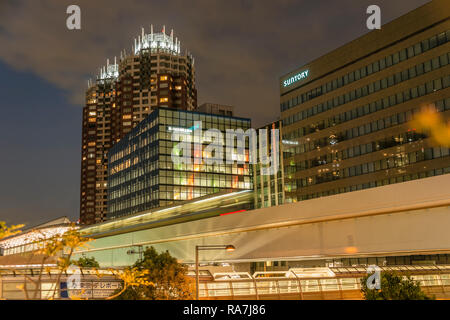 Tokyo Yurikamome Monorail Zug in Odaiba mit dem Suntory World Headquarter im Hintergrund bei Nacht, Japan Stockfoto