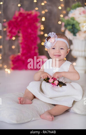 Cute Baby Mädchen 1-2 Jahre alten sitzen auf dem Boden mit rosa Luftballons im Zimmer über Weiß. Isoliert. Geburtstag. Feier. Happy birthday Baby, ein wenig Stockfoto