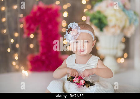 Cute Baby Mädchen 1-2 Jahre alten sitzen auf dem Boden mit rosa Luftballons im Zimmer über Weiß. Isoliert. Geburtstag. Feier. Happy birthday Baby, ein wenig Stockfoto