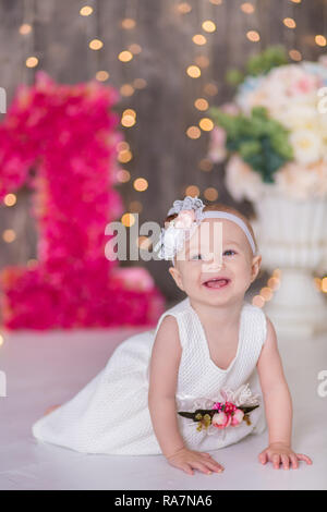 Cute Baby Mädchen 1-2 Jahre alten sitzen auf dem Boden mit rosa Luftballons im Zimmer über Weiß. Isoliert. Geburtstag. Feier. Happy birthday Baby, ein wenig Stockfoto