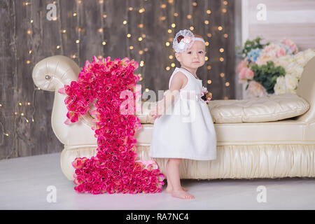 Cute Baby Mädchen 1-2 Jahre alten sitzen auf dem Boden mit rosa Luftballons im Zimmer über Weiß. Isoliert. Geburtstag. Feier. Happy birthday Baby, ein wenig Stockfoto