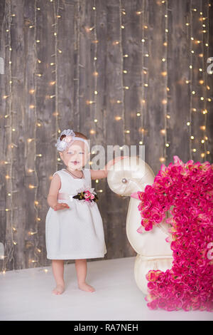 Cute Baby Mädchen 1-2 Jahre alten sitzen auf dem Boden mit rosa Luftballons im Zimmer über Weiß. Isoliert. Geburtstag. Feier. Happy birthday Baby, ein wenig Stockfoto