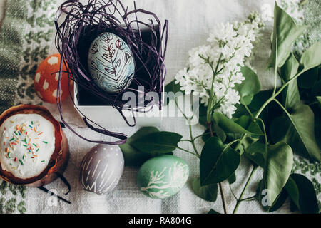 Ostern Kuchen und Ei im Nest mit floralen und chick Ornamente auf rustikalen Hintergrund mit lila Blumen. top anzeigen. Platz für Text. Frohe Ostern. Gruß Stockfoto