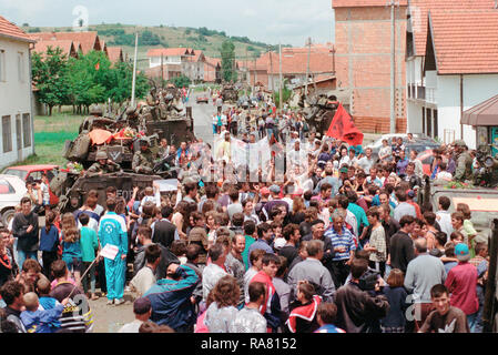 1999 - Ethenic Albaner versammeln sich in den Straßen für eine Parade statt die amerikanischen Streitkräfte im Kosovo Dorf Koretin zu ehren. Marines an Bord ihrer LAV-25, Leichte gepanzerte Fahrzeuge sind entlang der Straße Seite gesehen. Stockfoto