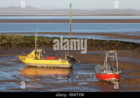 Zwei kleine Fischerboote, eine Gelbe und eine Rote, auf Schlamm bei Ebbe am Neujahrstag durch den Stein Mole in Morecambe, Lancashire, Großbritannien. Stockfoto