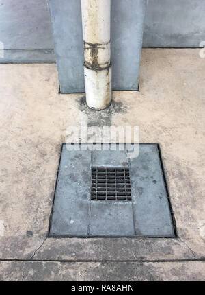 Metall Kanaldeckel auf dem Estrich in der Nähe die Ablaufleitung an der Wand fo der Fabrik. Stockfoto