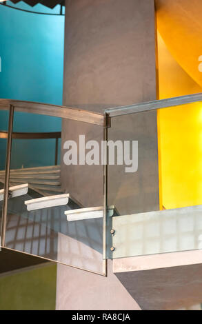 Bau Detail einer Wendeltreppe mit Geländer aus Stahl und Glas, die Wände in Blau, Gelb und Zement Stockfoto