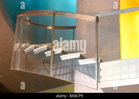 Bau Detail einer Wendeltreppe mit Geländer aus Stahl und Glas, die Wände in Blau, Gelb und Zement Stockfoto
