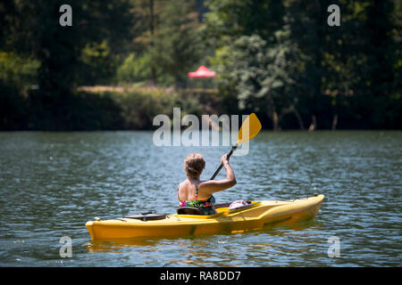Eine ältere gesunde Frau im Badeanzug sind Kajakfahren auf dem See Lacamas im grünen Wald, aktiv bewegen und entspannen an einem heißen Sommertag und Lo Stockfoto
