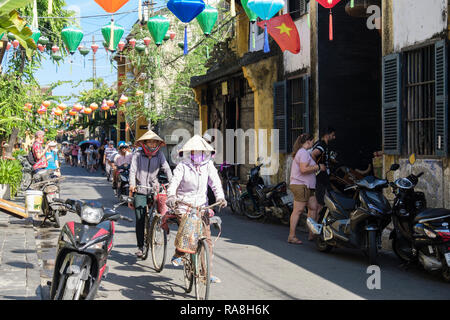 Typische Straßenszene mit einheimischen Frauen reiten Fahrräder in der Gasse in der Altstadt der historischen Stadt. Hoi An, Provinz Quang Nam, Vietnam, Asien Stockfoto