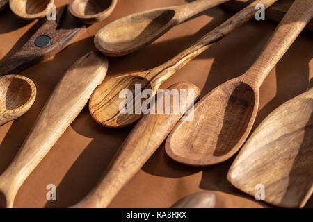 Löffel aus vielen verschiedenen Holzarten sitzen auf einem Tisch mit braunem Leder draußen in der Sonne abgedeckt Stockfoto