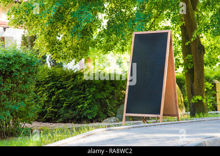 Eine leere Tafel Zeichen stehen auf der Straße, mit Pflanzen und Bäume um. Stockfoto