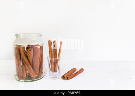 Zimt in Glas und Zimtstangen auf weissem Holztisch und weißem Hintergrund, Bild mit kopieren. Stockfoto