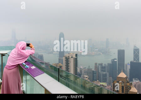 Frau nimmt ein Handy Foto auf dem Deck des Peak Tower Aussichtsplattform durch den Dunst aus der Luftverschmutzung eingeschränkt, Hong Kong Stockfoto
