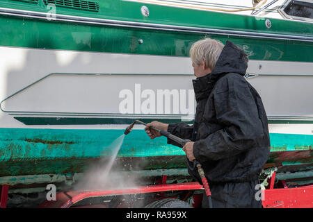 Kaukasische Mann mit schwarzen wasserdichten Anzug, während power Waschen schmutziger Bootsrumpf Stockfoto