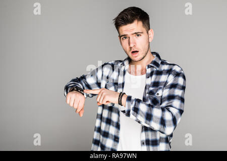 Jungen Mann im karierten Hemd auf Armbanduhr über grauen Hintergrund zeigend erstaunt Stockfoto