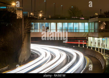 Lange Belichtung einer Autobahn Verkehr in der Nacht - leichte Wanderwege in den Schuß mit einer U-Bahn Station im Hintergrund gemalt. Stockfoto