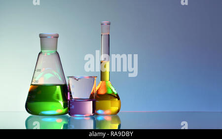 Laborglas mit bunten Flüssigkeiten und Chemikalien auf blauem Hintergrund Stockfoto